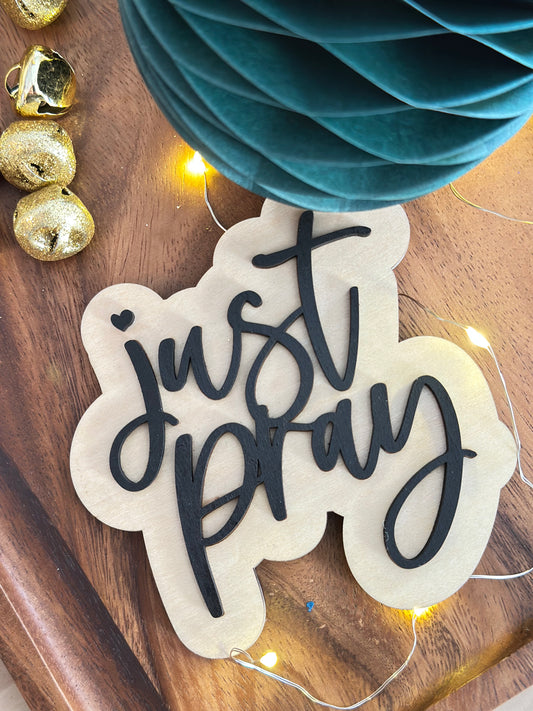 Decorative sign with 'just pray' text on a wooden surface with lights and decorations.